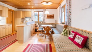 A cozy, well-lit kitchen with wooden cabinets, a dining area with a bench, and a sofa with decorative pillows. - Holiday Apartment in Kaltenbach (Kaltenbach)