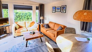 Ein modernes Wohnzimmer mit zwei Sofas, einem Couchtisch, einem Esstisch und einem großen Fenster mit Blick auf Grünflächen.