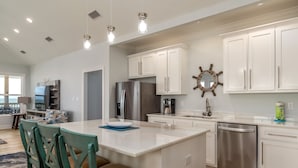 Cocina moderna con armarios blancos, un refrigerador de acero inoxidable y una isla central con taburetes de bar.