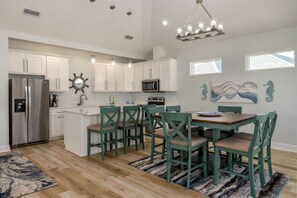 Eine moderne Küche mit weißen Schränken, einem Edelstahl-Kühlschrank, einer Mikrowelle und einem Essbereich mit türkisfarbenen Stühlen und einem Holztisch.