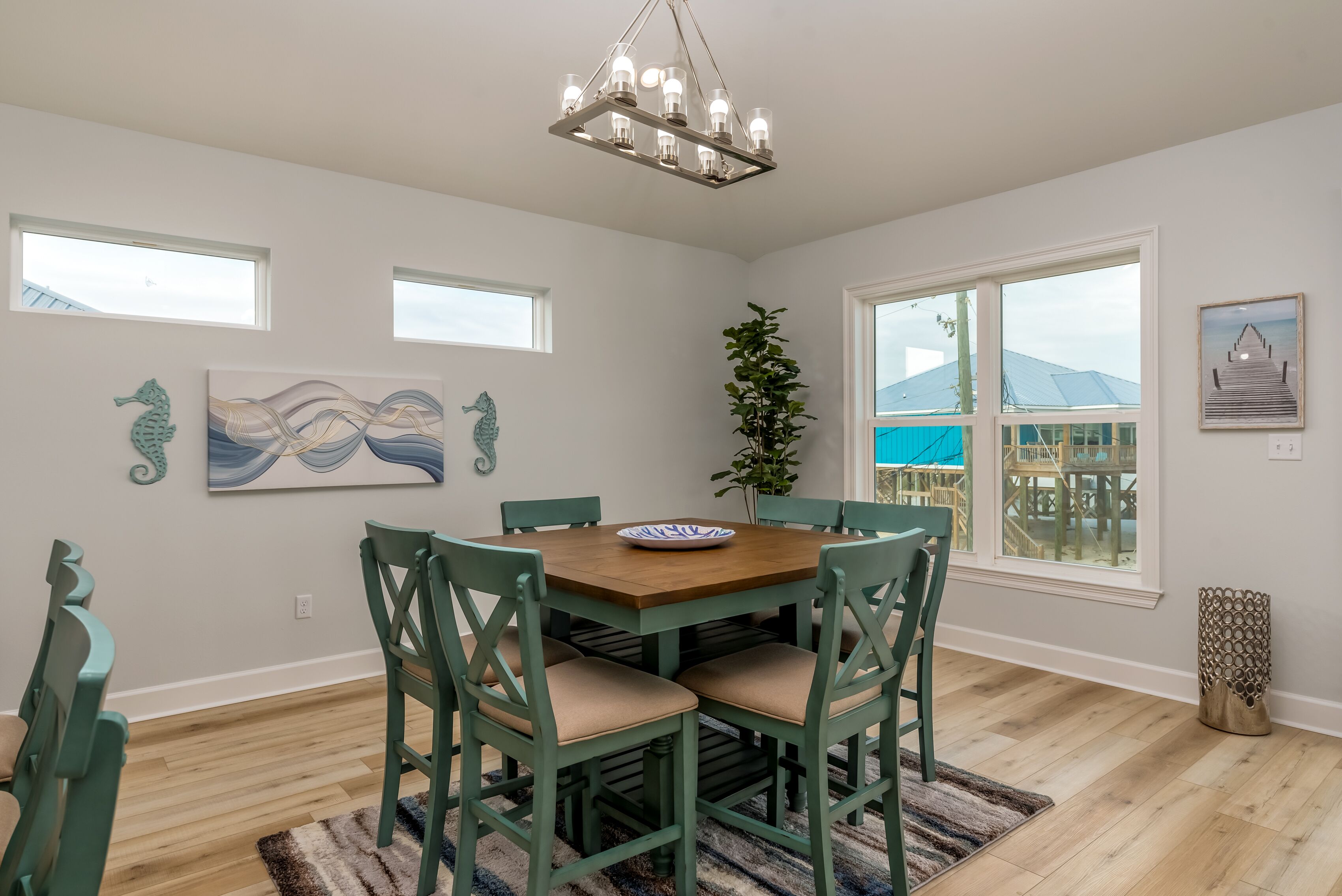 A dining area with a wooden table and green chairs, a chandelier, and artwork on the walls.
