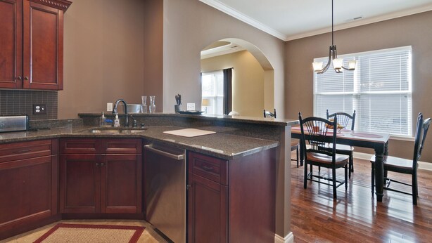A kitchen with dark wooden cabinets, a granite countertop, and a dining area with a table and chairs. - Lakes at Standifer Gap - Small subdivision close to Hamilton area, best shopping (Chattanooga)