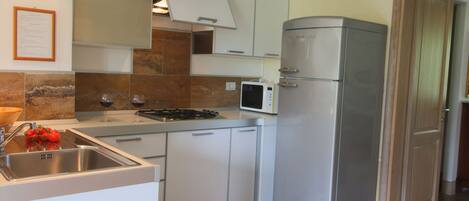 A compact kitchen with white cabinets, a stainless steel refrigerator, a microwave, and a gas stove.