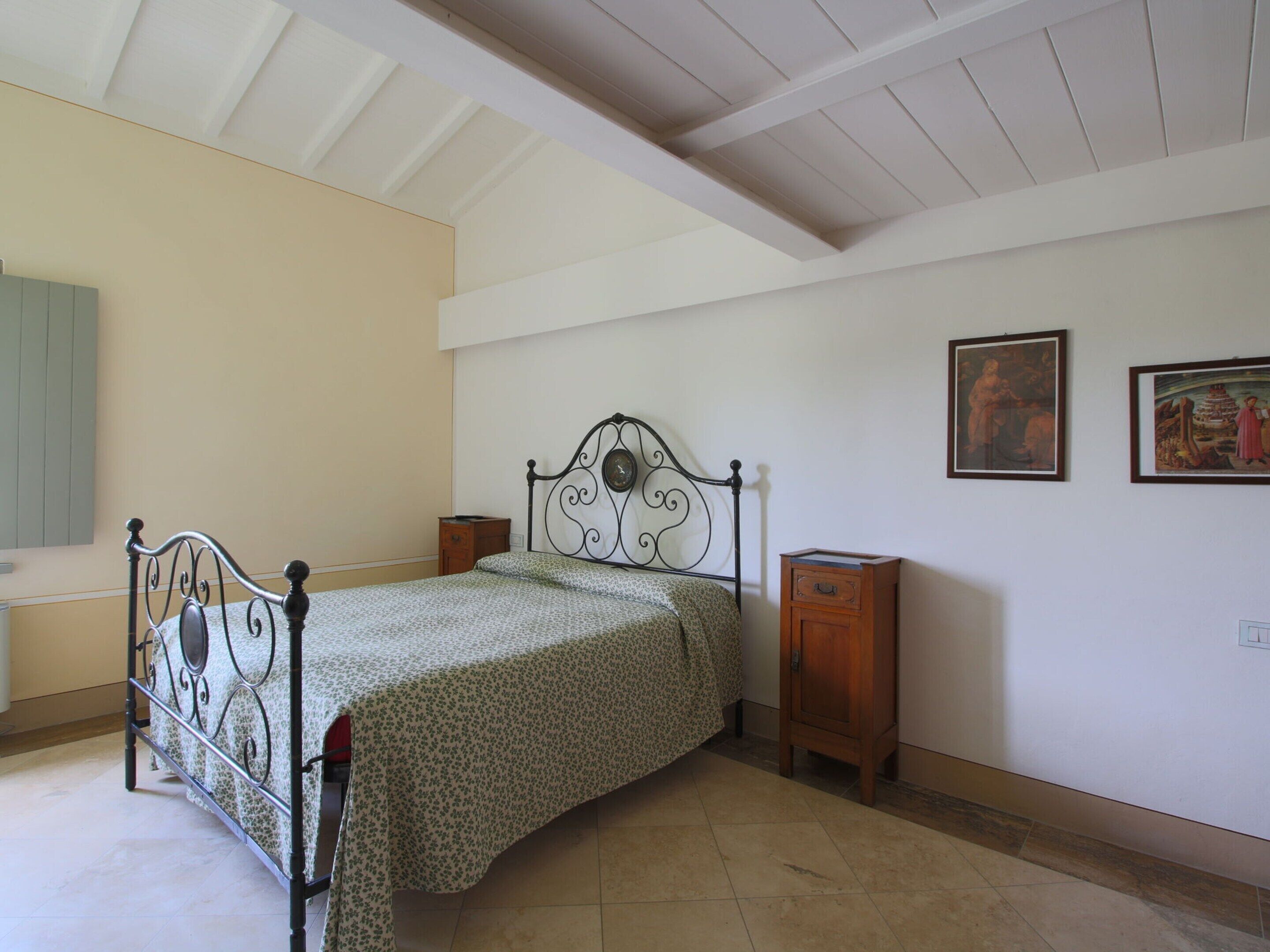 Un dormitorio con cama, mesita de noche y dos cuadros colgados en la pared.