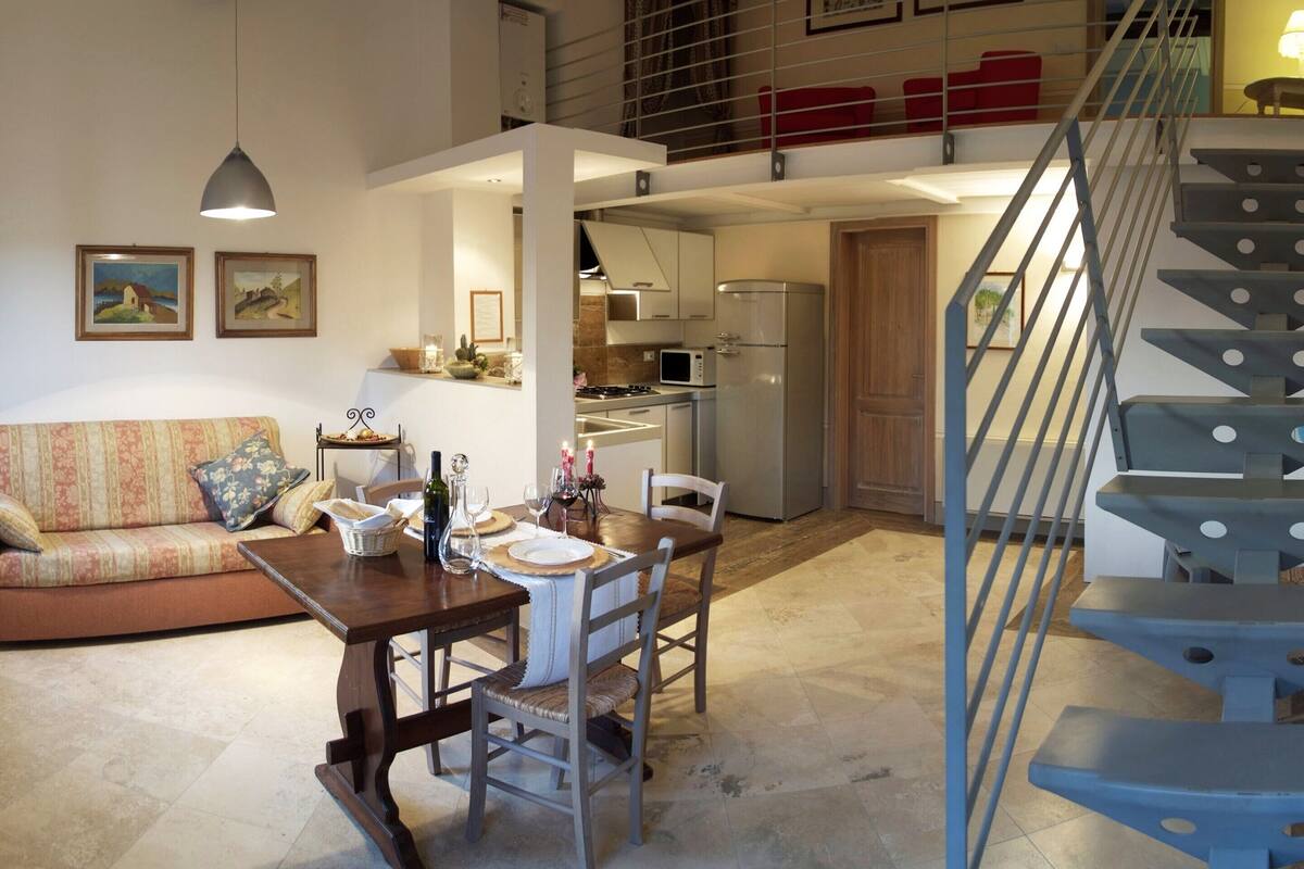 A spacious living area with a dining table set for four, a sofa, and a staircase leading to an upper level.