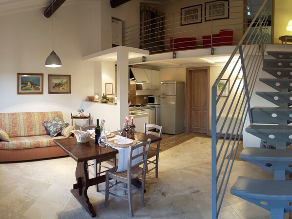 A spacious living area with a dining table set for four, a sofa, and a staircase leading to an upper level.