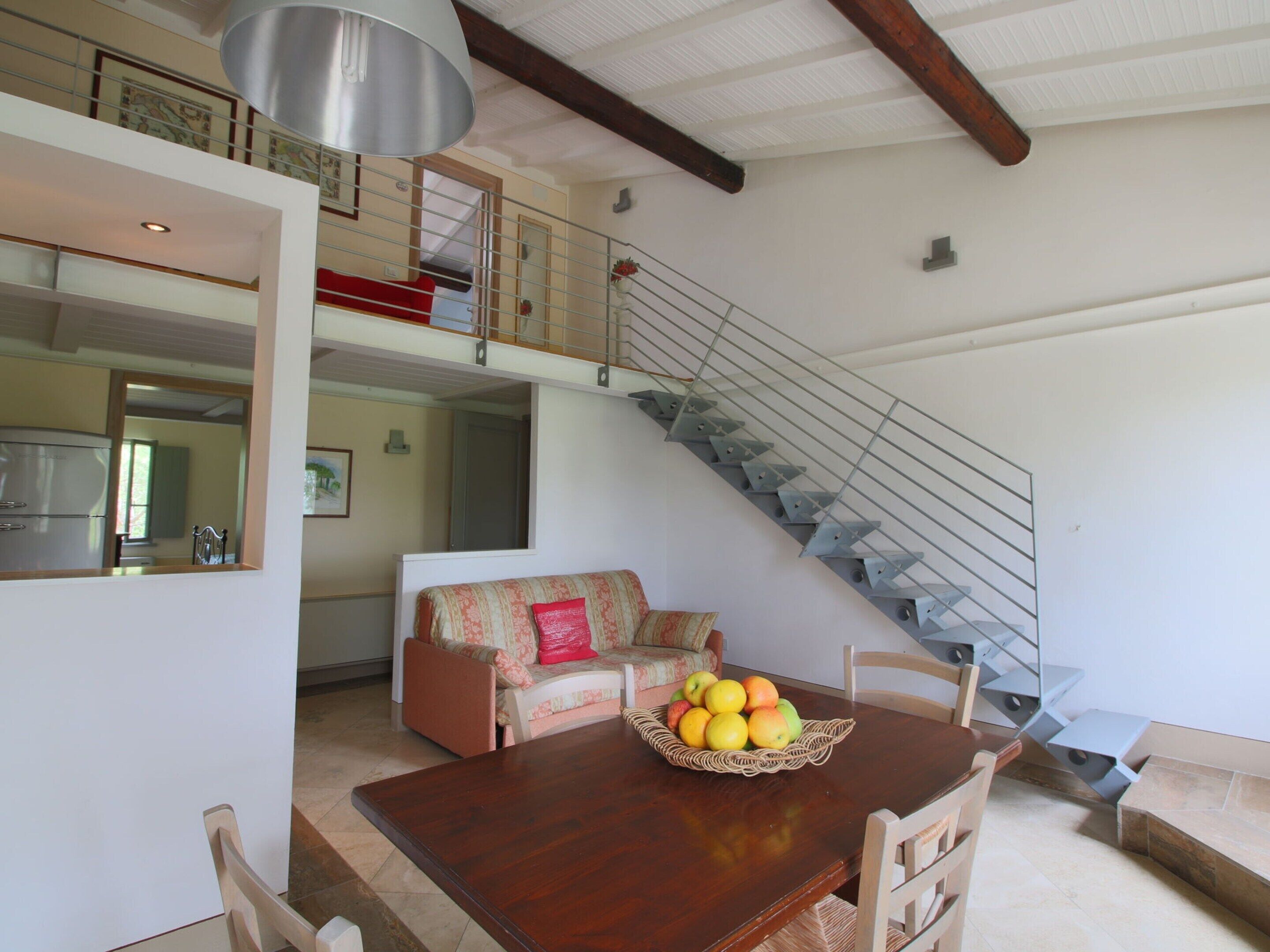 Un comedor con una mesa y sillas de madera, una cesta de fruta, una escalera y un sofá rojo.
