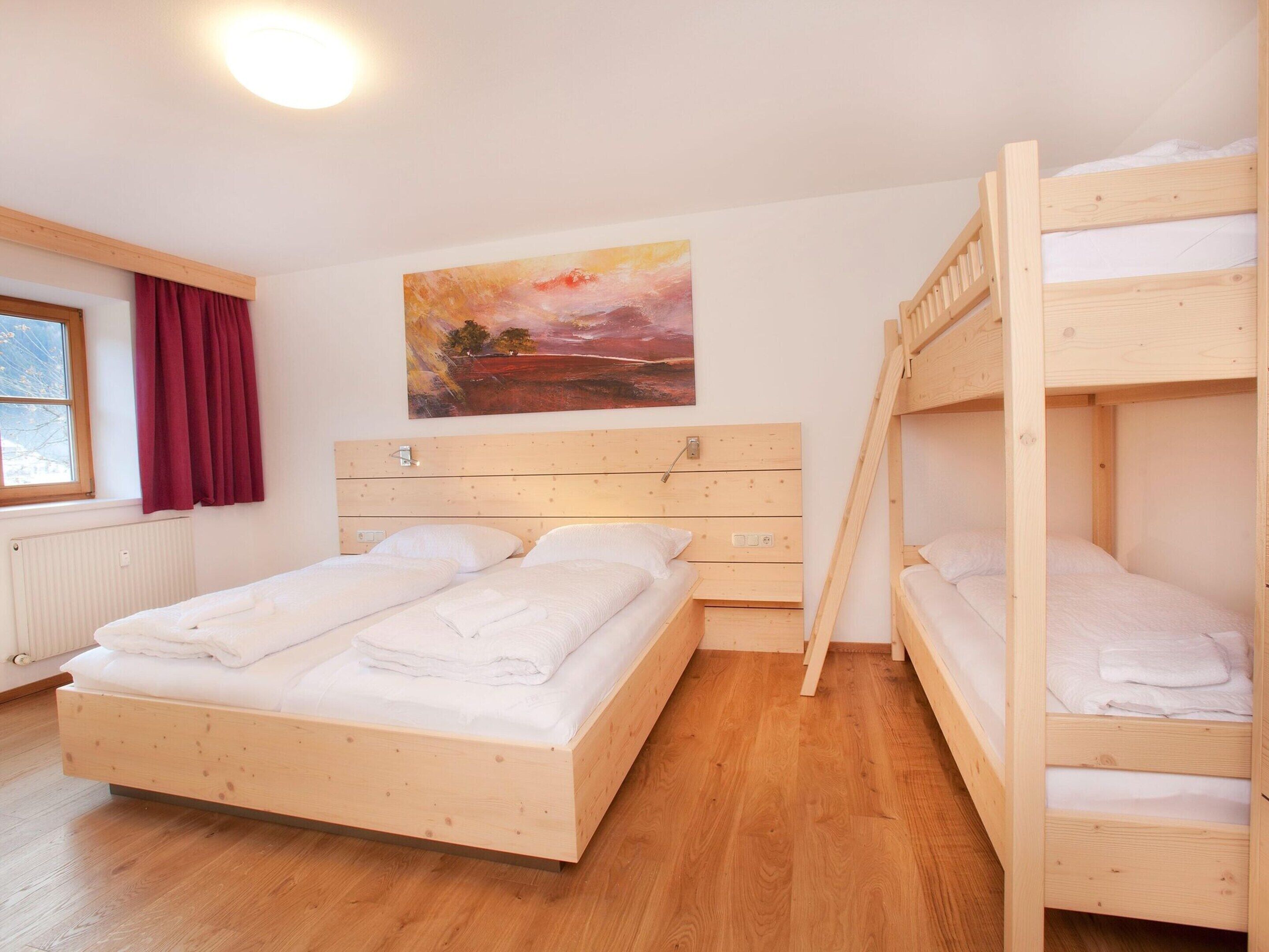 A room with a wooden bunk bed, a single bed, and a painting on the wall.