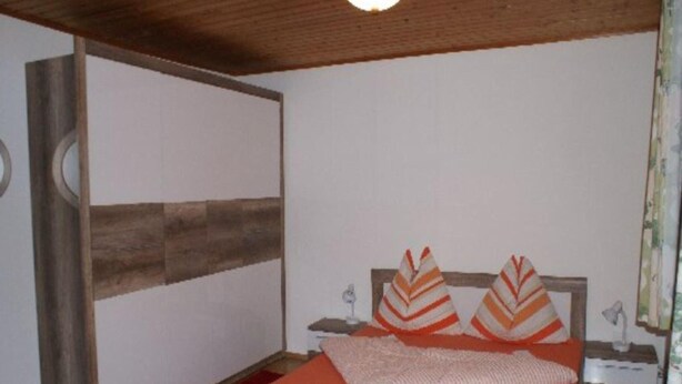 Ein Schlafzimmer mit einem hölzernen Bett, einem roten Teppich und einer weißen Wand mit einer Holzvertäfelung.