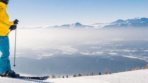 Eine Person fährt auf einem verschneiten Hang mit freiem Blick auf ferne Berge und ein Tal.
