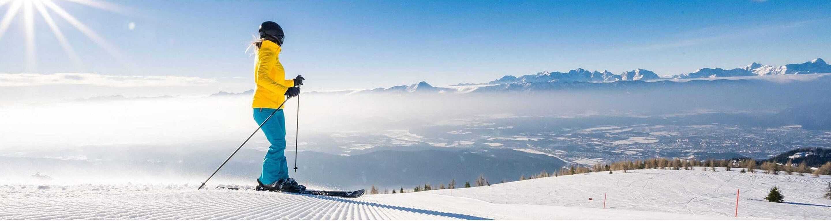 Une personne fait du ski sur une pente enneigée, avec une vue sur des montagnes lointaines et un ciel dégagé.