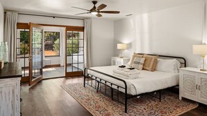 Un dormitorio con cama, mesitas de noche, ventilador de techo y vistas al exterior por una puerta de vidrio.