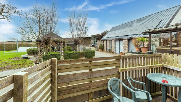 A wooden deck with a table and chairs, a brick building with a metal roof, and a green lawn. - Zoutleeuw Home With Pool (Zoutleeuw)