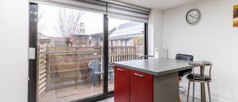 A kitchen with a sliding glass door, a red cabinet, a bar stool, and a clock on the wall.