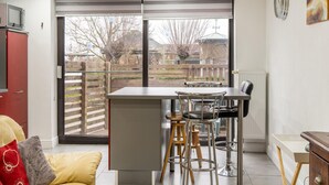 A modern kitchen with a large window, a dining area with stools, and a red cabinet. - Zoutleeuw Home With Pool (Zoutleeuw)