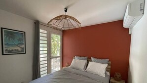 A bedroom with a bed, a window with curtains, a wall-mounted air conditioner, and a framed picture on the wall. - Kay Agapi - on the beach - Diamant (Le Diamant)