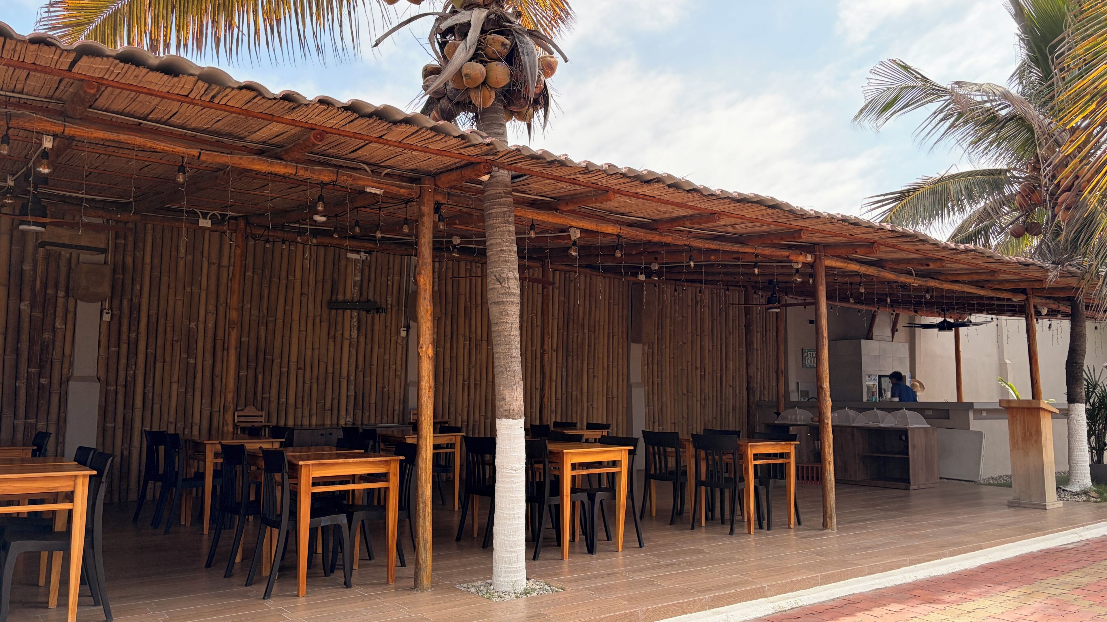 An outdoor restaurant with bamboo walls, wooden tables, and chairs.