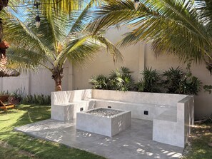 A modern outdoor seating area with a concrete bench and a fire pit, surrounded by palm trees and other greenery. - La Mar Hotel Playas (Playas)