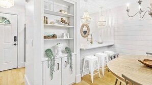 A modern kitchen with white cabinetry, a wooden dining table, white bar stools, and pendant lights. - Luxury Townhouse in Santa Rosa Beach - The Zen Pad (Santa Rosa Beach)
