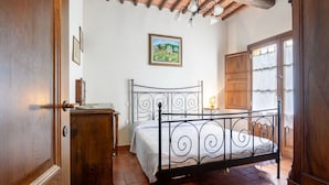 Un dormitorio con estructura de cama de metal, un armario de madera, un escritorio con lámpara y un cuadro en la pared.