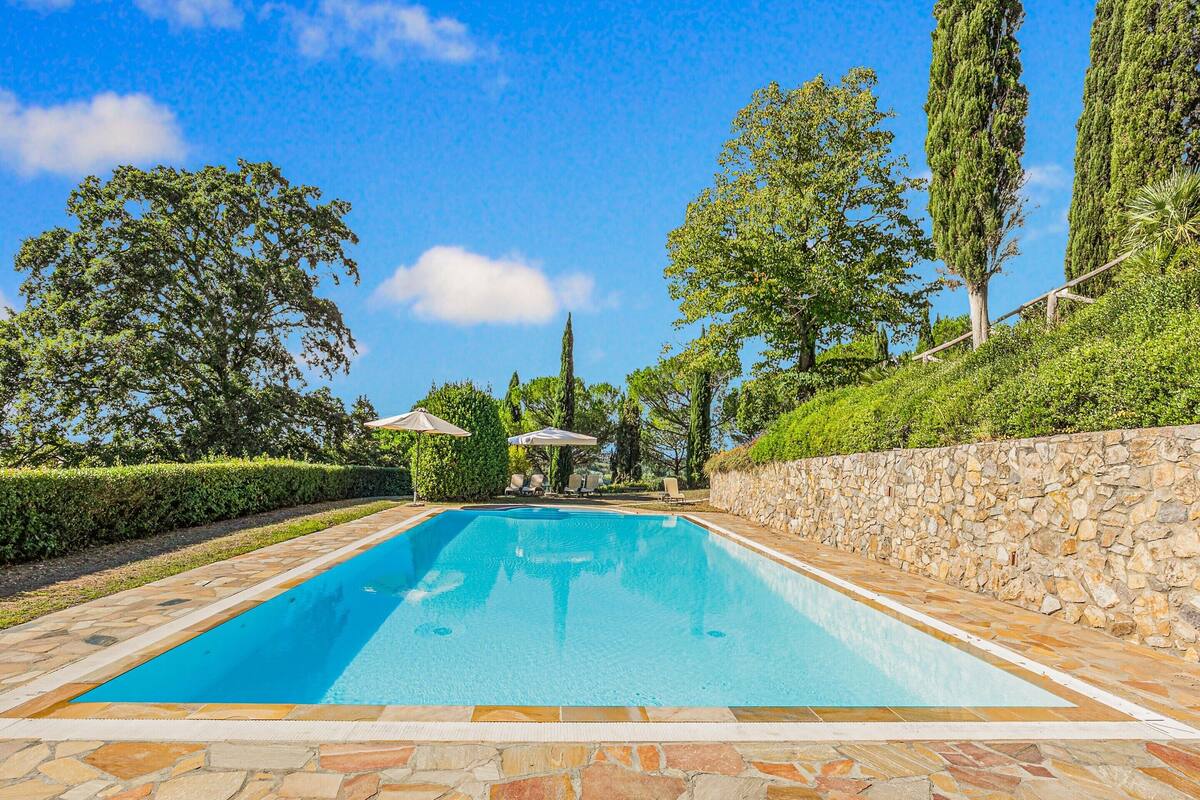 Ein rechteckiger Pool mit Steinplatten, umgeben von einer Steinmauer und Bäumen.