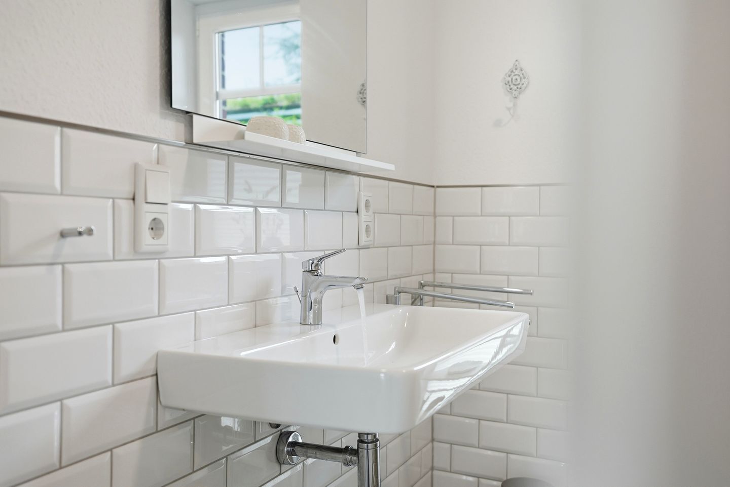 A bathroom with white tiled walls, a white sink, a chrome faucet, and a mirror above the sink.