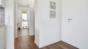 A hallway with a white door, a light switch, and a wall-mounted light fixture. - Lieblingsort - Neubauwohnung mit Hund für bis zu 4 Personen im Greetsieler Grachtenpark (Krummhörn)