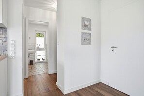 Un couloir avec une porte blanche, un interrupteur et un luminaire fixé au mur.