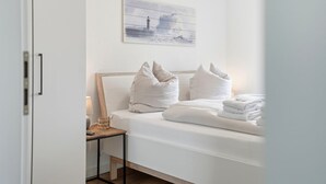 Ett hotellrum med en säng, kuddar, ett sängbord med en lampa och en tavla på väggen.