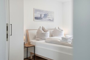 A hotel room with a bed, pillows, a bedside table with a lamp, and a painting on the wall. - Lieblingsort - Neubauwohnung mit Hund für bis zu 4 Personen im Greetsieler Grachtenpark (Krummhörn)