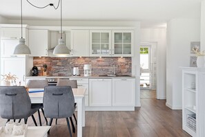 A modern kitchen with white cabinetry, a stone backsplash, and a dining area with grey chairs. - Lieblingsort - Neubauwohnung mit Hund für bis zu 4 Personen im Greetsieler Grachtenpark (Krummhörn)
