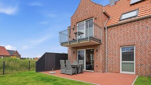 Ett hus byggt av tegel med en balkong, en inhägnad trädgård och en uteplats med utemöbler.