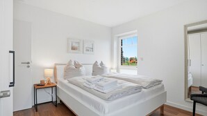 A bedroom with a bed, bedside table, lamp, and a window with a view of the outside. - Lieblingsort - Neubauwohnung mit Hund für bis zu 4 Personen im Greetsieler Grachtenpark (Krummhörn)