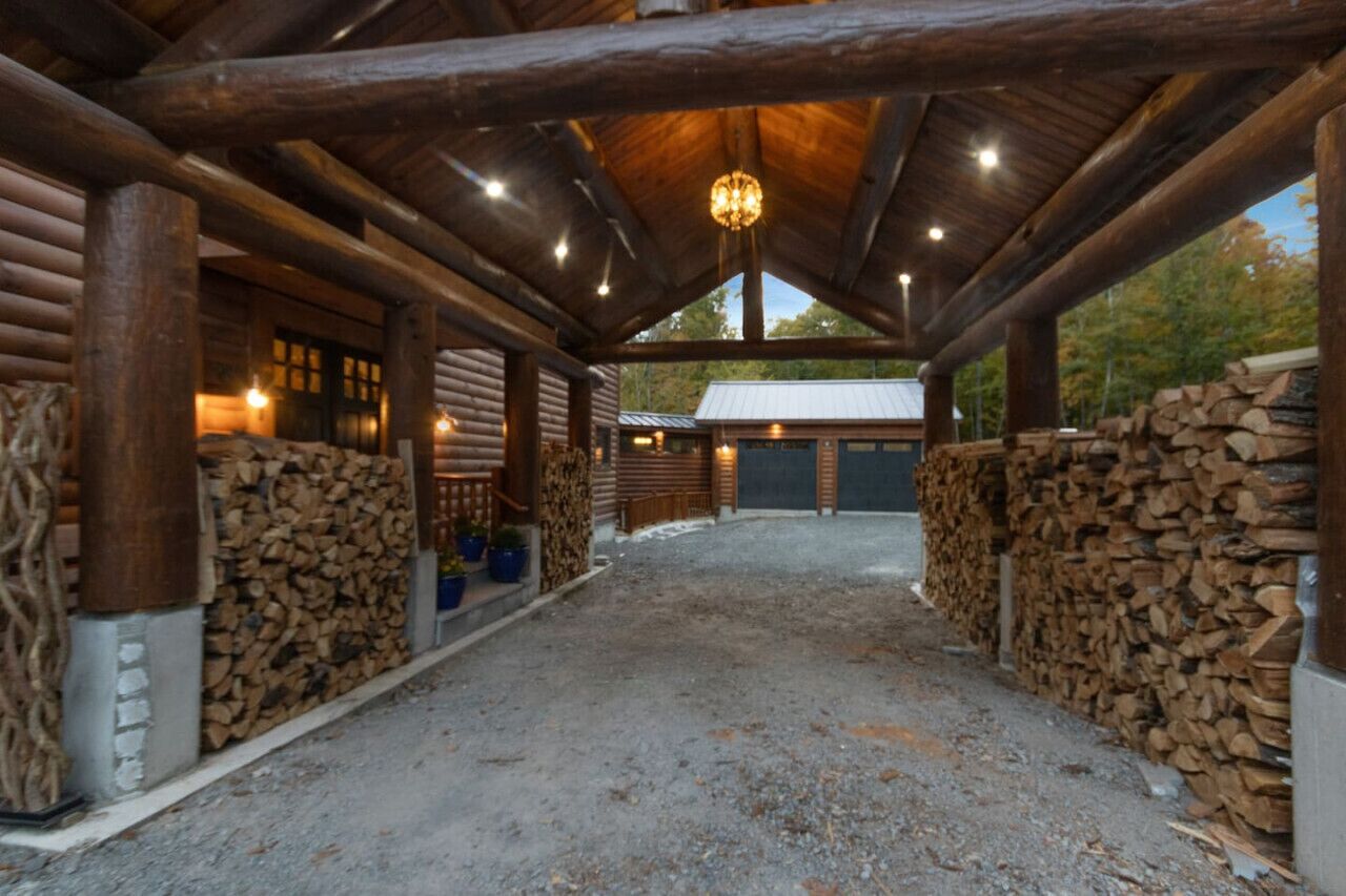 A log cabin with a covered porch, wooden walls, and a gravel driveway.