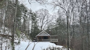 Een chalet met een houten gevel, een veranda en een oprit vol sneeuw.