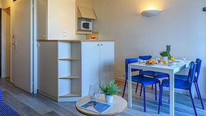 Kompakti keittiö, jossa on mikroaaltouuni, ruokapöytä tuoleineen ja pieni ruukkukasvi pöydällä.