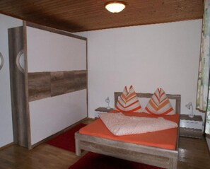 Un dormitorio con estructura de cama de madera, colcha roja y dos almohadas decorativas.