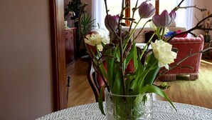 Een woonkamer met een ronde tafel, een vaas met bloemen, een rode fauteuil en een houten vloer.