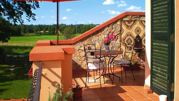 Een terras met een tafel en stoelen, een rode parasol en een stenen muur met een decoratief tegeltapijt.