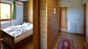 Ein Zimmer mit Holzwänden, einem Bett, einem Heizkörper und einer Tür zu einem weiteren Raum.