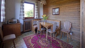 Ein gemütliches Zimmer mit Holzwand, einem Esstisch mit Stühlen, einem Heizkörper und einem Fenster mit Vorhängen.