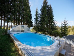 A swimming pool with a glass enclosure, surrounded by tall trees and a clear sky. - Apartment in Fresach Near Millstattersee With Pool (Fresach)