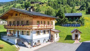 A two-story wooden house with a balcony, a small attached building, and solar panels in a rural setting. - Elegant Apartment Near the ski bus (Saalbach-Hinterglemm)