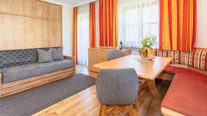 A modern living room with a sofa, a dining table, and a wooden cabinet. - Elegant Apartment Near the ski bus (Saalbach-Hinterglemm)