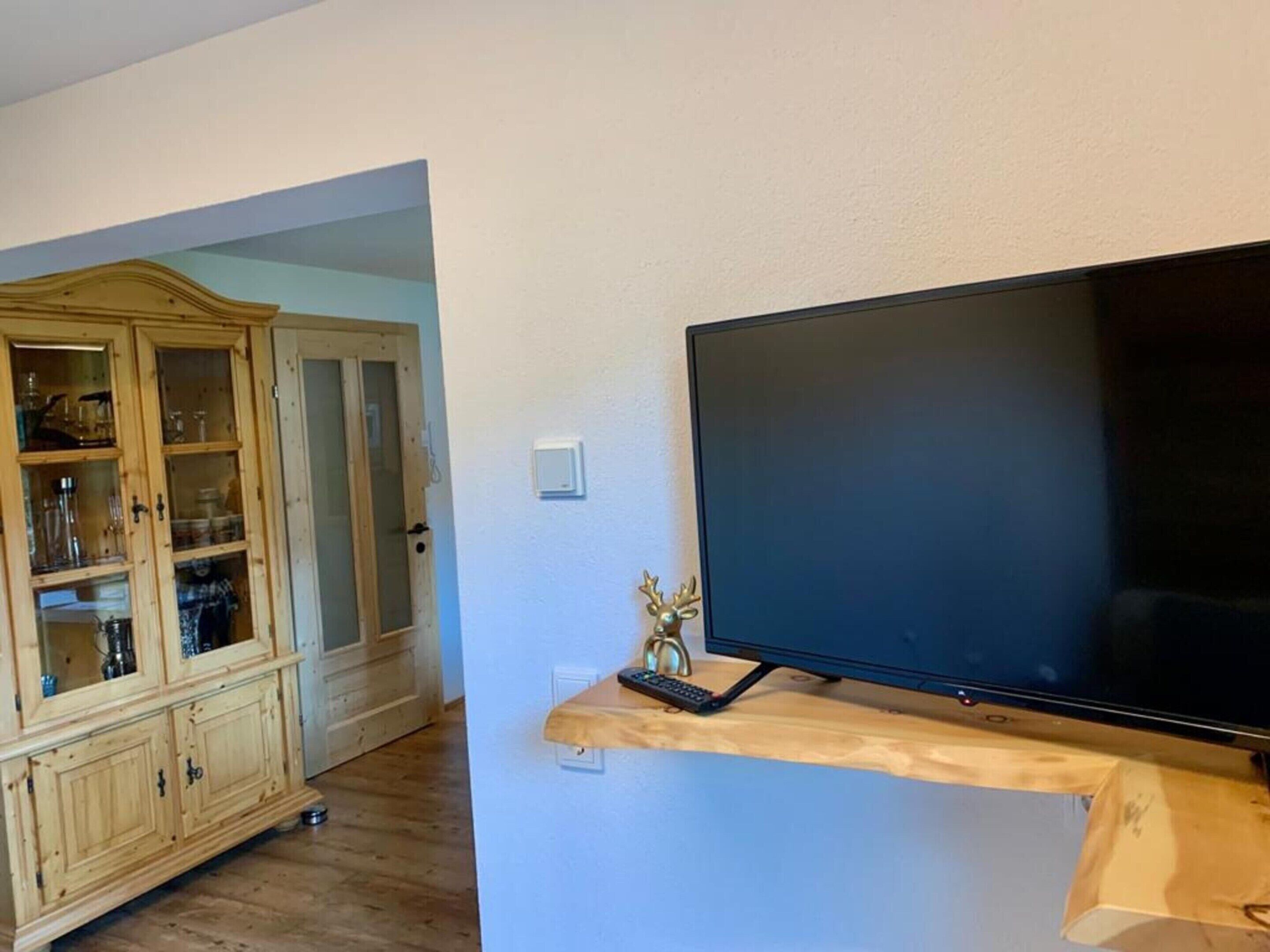 A room with a wooden cabinet containing glassware and a television on a wooden stand.