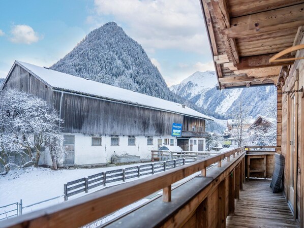 A wooden building with a snow-covered roof, a wooden deck, and a mountain in the background.