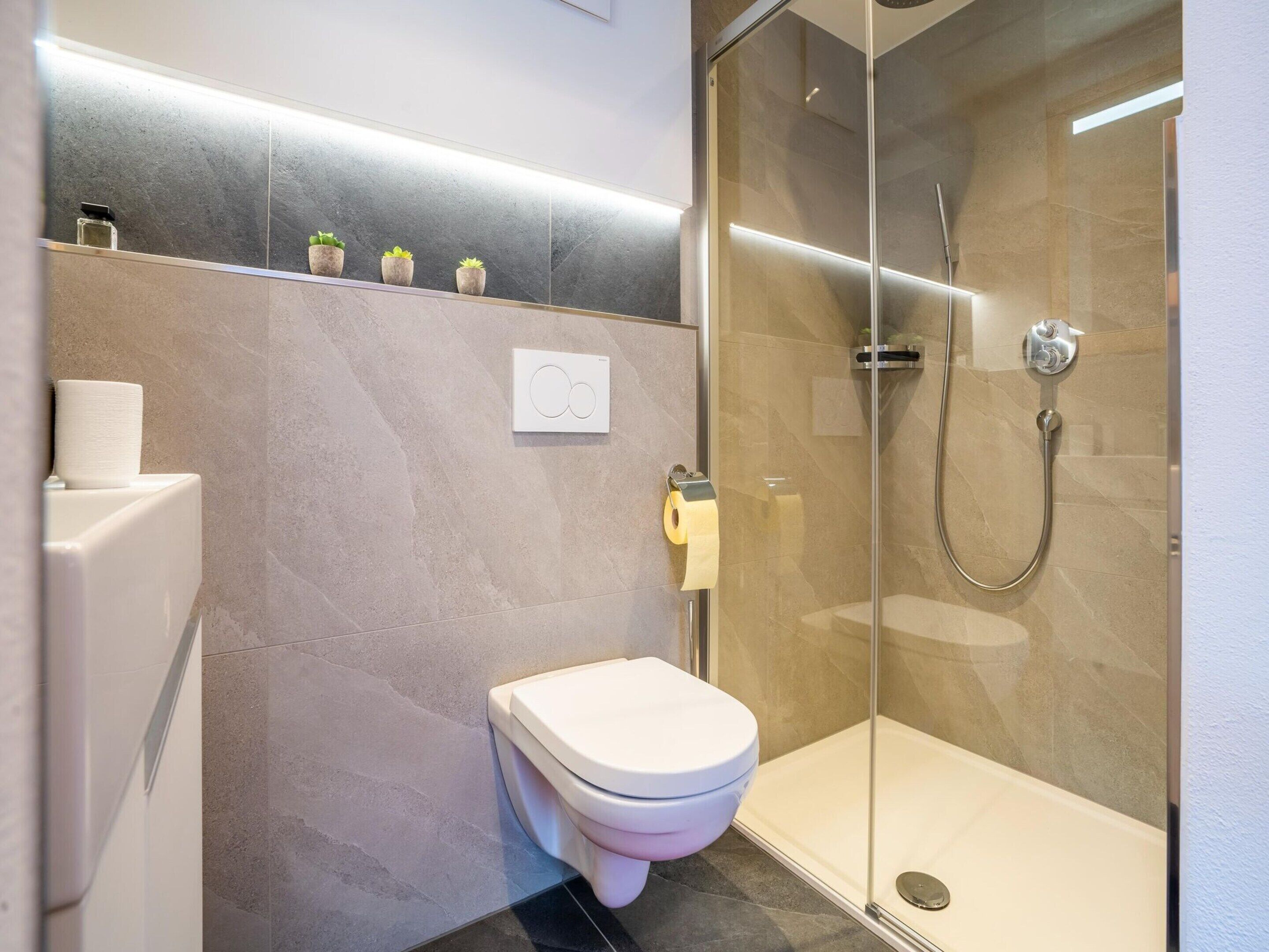 Une salle de bain moderne avec des toilettes, une douche en verre et un mur recouvert de carreaux de marbre.