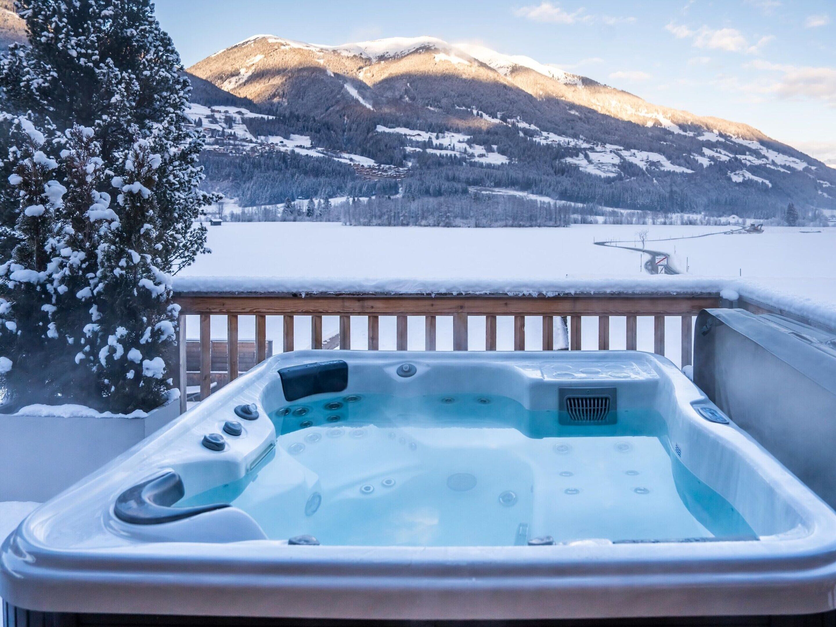 Ein Whirlpool auf einer Holterrasse mit verschneiter Landschaft und Bergen im Hintergrund.