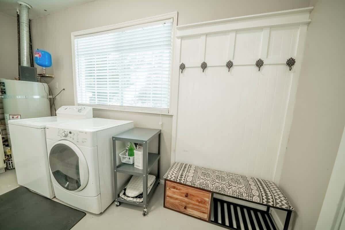 A laundry room with a washing machine, a drying rack, a small shelf with bottles, and a bench with a patterned cushion.