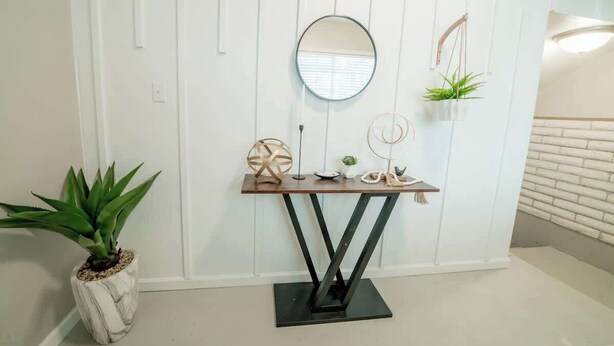 A white wall with a wooden console table, a round mirror, and a hanging plant.